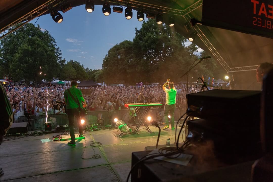 Band performing on stage in front of a large crowd at dusk